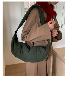 Detail of dark green quilted nylon crescent bag worn over a camel trench coat