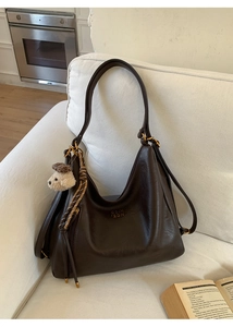 Detail of a dark brown soft leather tote bag with gold hardware and plush bear charm
