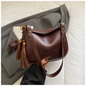 Détail macro du sac selle en cuir rouge vin avec de longs glands et ferrures dorées