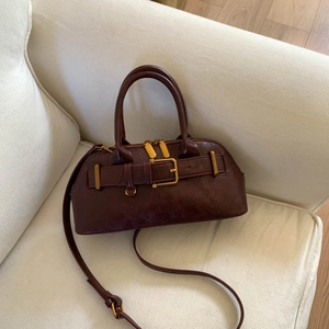Detail of burgundy retro handbag with gold metal buckles on a soft white sofa