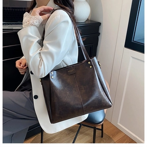 Detailed close-up of dark brown vintage faux leather tote with gold rivets and brand logo