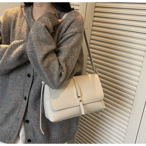 Detail of creamy white leather shoulder bag featuring rich pebble texture and gold buckle