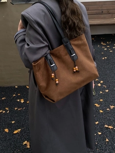 Dettaglio di una borsa tote in pelle scamosciata marrone con cinturini neri e ciondoli vintage