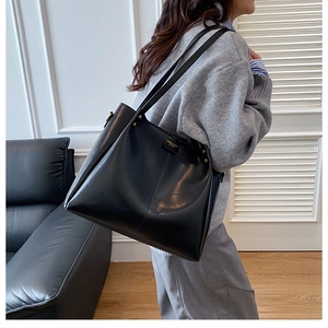 Side view of large black matte leather tote bag worn as a stylish underarm shoulder bag