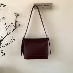 Detail der burgunderroten Leder-Eimertasche an der Wand mit dekorativem Riemen