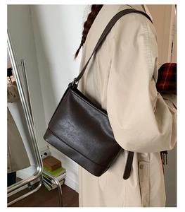 Detail einer dunkelbraunen matten Leder-Eimertasche getragen mit einem beigen Trenchcoat