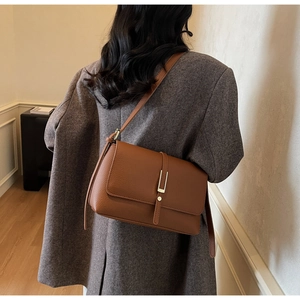 Close-up of brown textured leather crossbody bag with elegant gold buckle on model