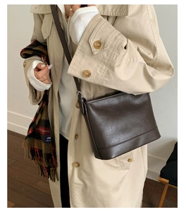 Dunkelbraune matte Beuteltasche an Model mit beigem Herbst-Trenchcoat für einen Retro-Look