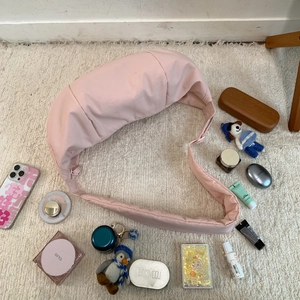 Flat lay of pink nylon crescent bag with daily essentials on soft cream carpet