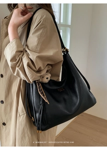 Detail of black leather tote bag with plush bear charm and tassel on khaki trench coat
