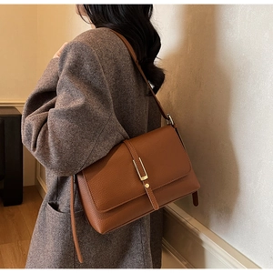 Detail of a brown leather shoulder bag with a gold metal buckle on a tweed coat