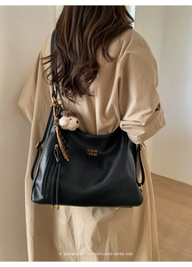 Detail view of retro black leather tote bag featuring golden logo and bear pendant
