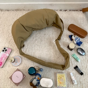 Spacious khaki nylon dumpling bag shown with various daily items on a soft white rug