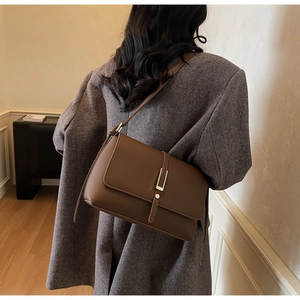Detail of vintage brown leather bag with lychee texture and gold metal clasp on model