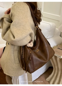 Detail of dark brown faux leather hobo bag with gold logo lettering and bear charm