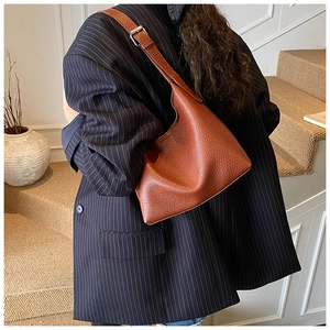 Brown lychee leather bucket bag shown on shoulder with minimalist pebble texture and silver buckle