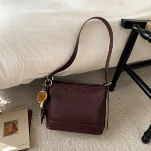 Detail der burgunderroten Schultertasche mit Pilzanhänger auf weißem Bettzeug