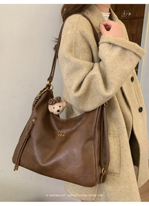 Detail of dark brown leather tote bag with metal logo and cute bear charm accessory