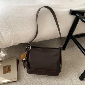 Detailansicht einer dunkelbraunen Beuteltasche mit Baseball-Anhänger auf einem Teppich