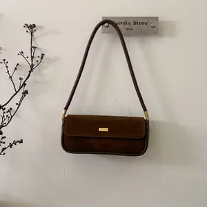 Detail einer braunen Wildleder-Achseltasche mit goldener Metallschnalle und Schultergurt