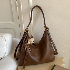 Detail view of brown vintage PU leather tote bag with a knitted bear charm and gold hardware
