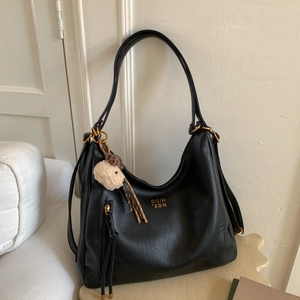 Detail of black vintage tote bag featuring gold logo, side tassel, and plush lamb charm