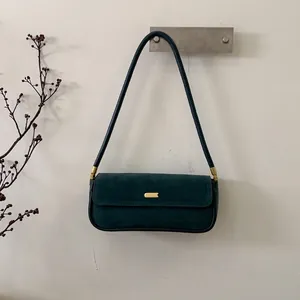 Detail einer dunkelgrünen Wildleder-Baguette-Tasche mit eleganter Goldmetallschnalle