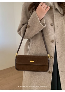 Détail d'un sac baguette rétro en daim marron avec boucle dorée sur manteau laine