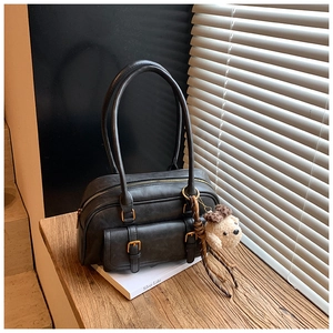 Close-up of black retro bowling bag with gold hardware and plush charm on wood table