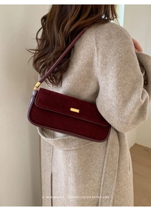 Gros plan d'un sac à bandoulière rétro en cuir bordeaux sur un manteau en laine