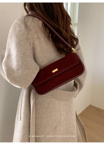Détail du sac baguette en daim bordeaux avec boucle dorée sur l'épaule du mannequin