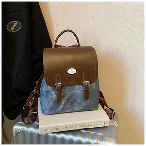 Detail eines blauen Denim-Rucksacks mit braunem Lederbesatz und Hasen-Emblem auf Koffer