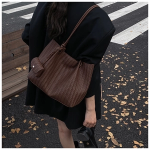Detail shot of a dark brown woven tote bag with a matching mini pouch on a long shoulder strap