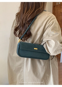 Détail du sac sous le bras en daim vert foncé avec boucle dorée et design rétro épuré