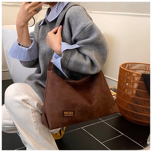 Détail d'un sac cabas en daim marron foncé avec une plaque de marque métallique en intérieur