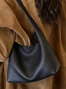 Minimalist black pebble leather bucket hobo bag worn as a shoulder bag for daily commute