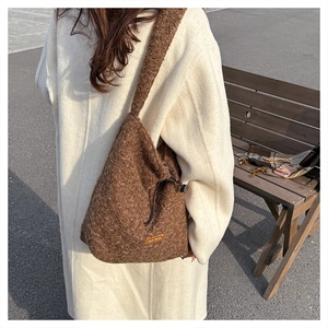 Detail of a brown faux fur crossbody bag with side drawstring and orange woven label tag