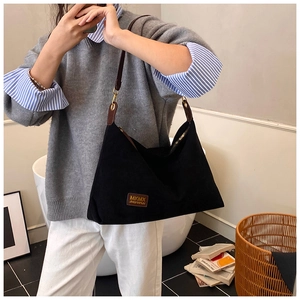 Détail du sac cabas en toile noire avec étiquette en cuir brun et boucle métallique dorée