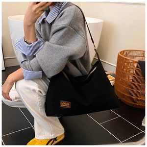 Détail du grand sac cabas en toile noire montrant l'étiquette logo en cuir et la bandoulière