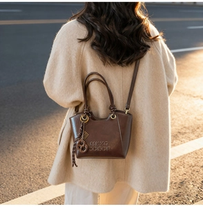 Détail d'un sac seau marron foncé avec logo en relief et breloque tressée au coucher du soleil