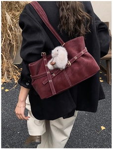 Detail of burgundy suede tote with white stitching, decorative belts and rabbit charm
