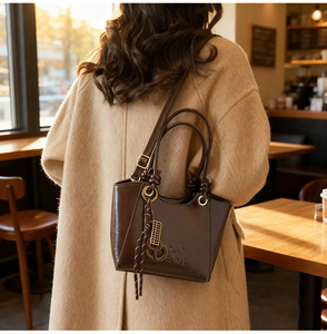 Détail du sac seau en cuir marron foncé avec anneau métallique et pompon élégant