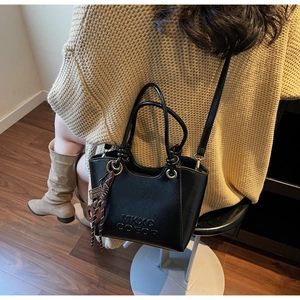 Détail d'un sac seau noir brillant avec logo MKXQ COEOR et breloque à franges marron