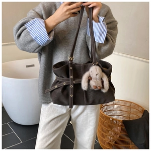Detail of a dark brown pleated tote bag with contrast stitching and rabbit plush charm