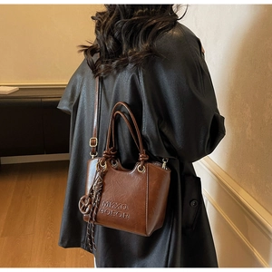 Détail du sac seau vintage marron foncé avec logo embossé et breloque tressée élégante