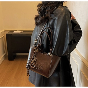 Détail d'un sac seau vintage en cuir brillant marron foncé avec pompons et bandoulière