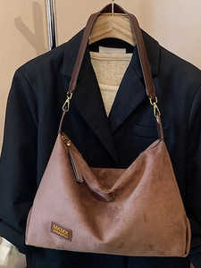 Sac hobo en daim marron avec bandoulière en cuir suspendu sur un blazer noir élégant