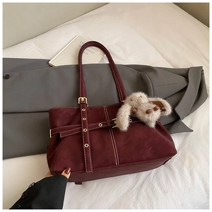 Detail of burgundy suede tote bag with metal buckles and a plush rabbit charm