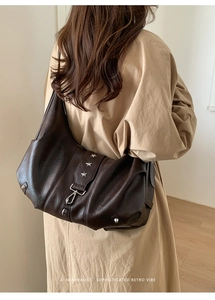 Detail of soft brown leather tote with star rivet and metal buckle on trench coat