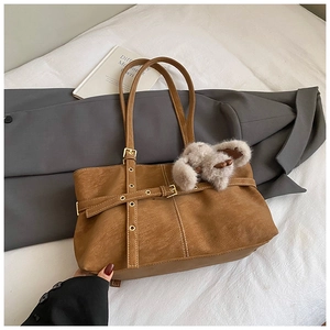 Brown faux suede tote bag with belt buckle detail and plush bunny charm on bed